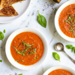 Pinterest Pin with text 'Roasted Red Pepper & Tomato Soup, easy and healthy with fresh vegetables' image of three white bowls of tomato soup with basil leaves.