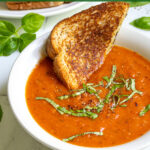 Pinterest Pin with text 'easy and healthy Roasted Red Pepper & Tomato Soup' image of a white bowl of tomato soup with basil leaves.