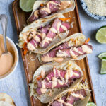 Pinterest Pin with text overlay 'Tuna Steak Tacos with sriracha mayo & asian slaw' images of a tray full of seared tuna tacos with garnishes.