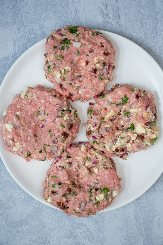 Raw greek turkey burgers on a plate with all the mix-ins visible.