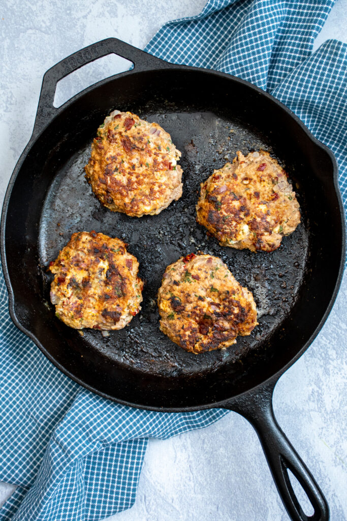 Skillet with 4 greek turkey burgers just cooked.