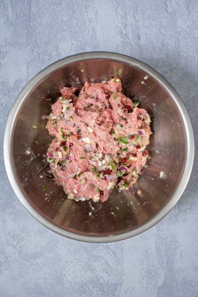 A stainless steel bowl filled with the raw mixture for Mediterranean turkey burgers.