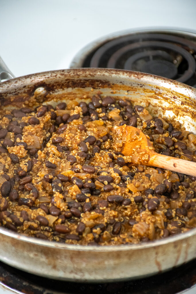 A skillet with cooked black beans and quinoa to be used as a flavorful taco meat.