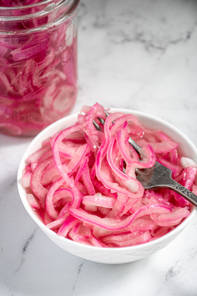 Close up of a white bowl filled with quick pickled onions and a fork.