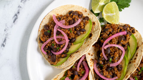 Overhead view of a white plate filled with black bean quinoa tacos garnished with cilantro, pickled onions, and avocado.