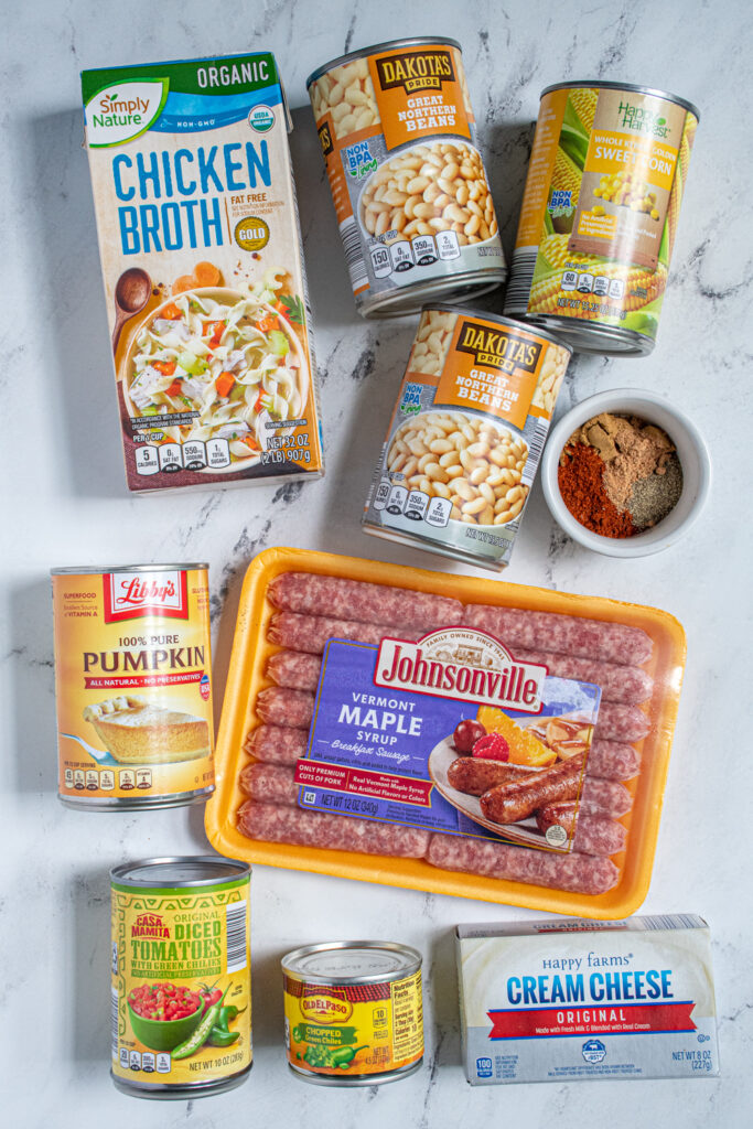 Ingredients to make creamy pumpkin chili in the crockpot laid out on a countertop including maple sausages, white beans, and pumpkin puree.