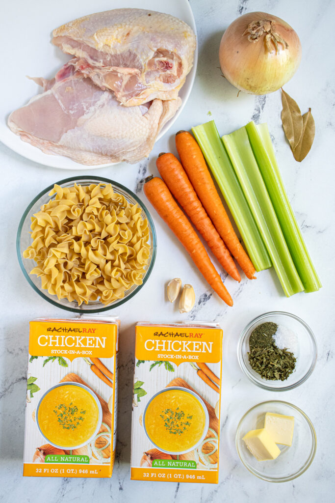 Ingredients needed to make easy chicken noodle soup including split chicken breasts, veggies, and egg noodles.