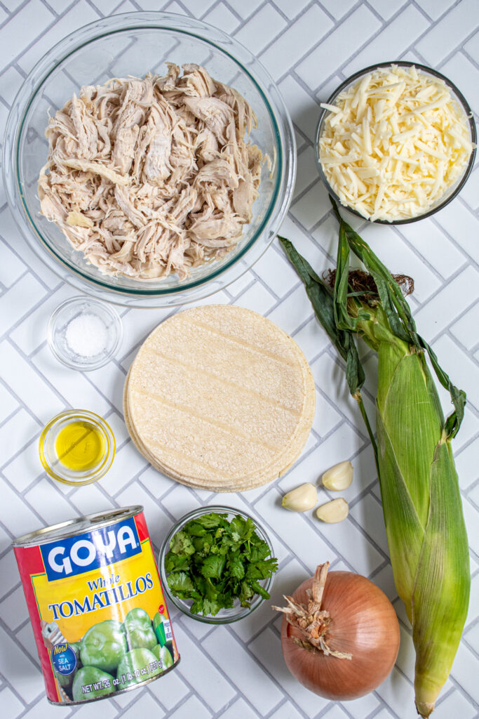Ingredients needed to make green chicken enchiladas laid out on a counter top, including tomatillos and shredded chicken.
