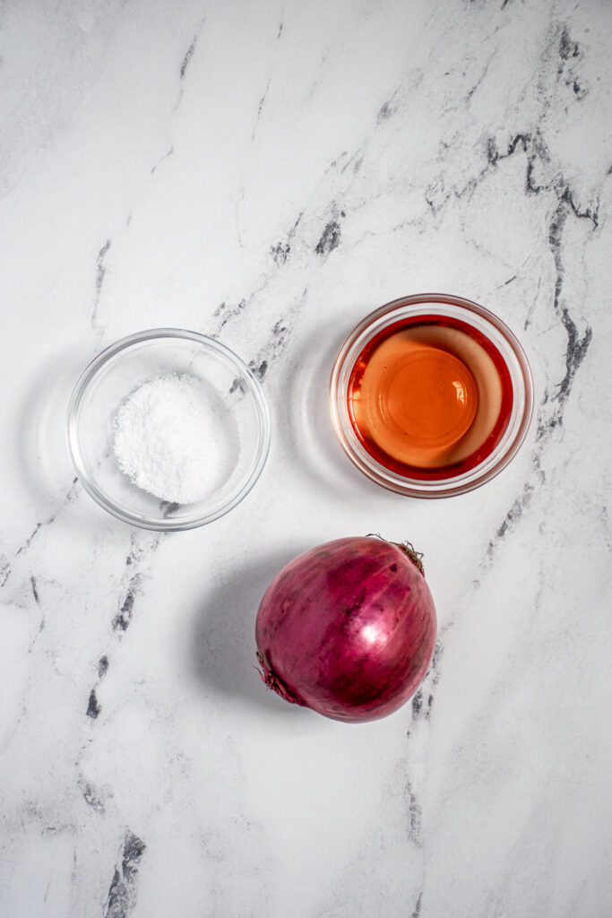 Ingredients for making quick pickled onions including a red onion, salt, and red wine vinegar.
