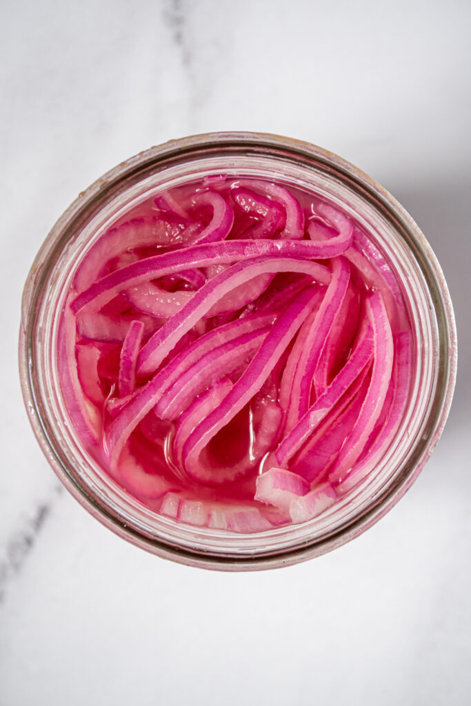 A close up of a wide mouth jar showing bright red pickled onions.