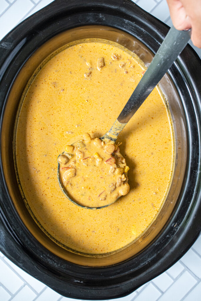 A black crockpot with cooked pumpkin chili and a paddle holding some up.