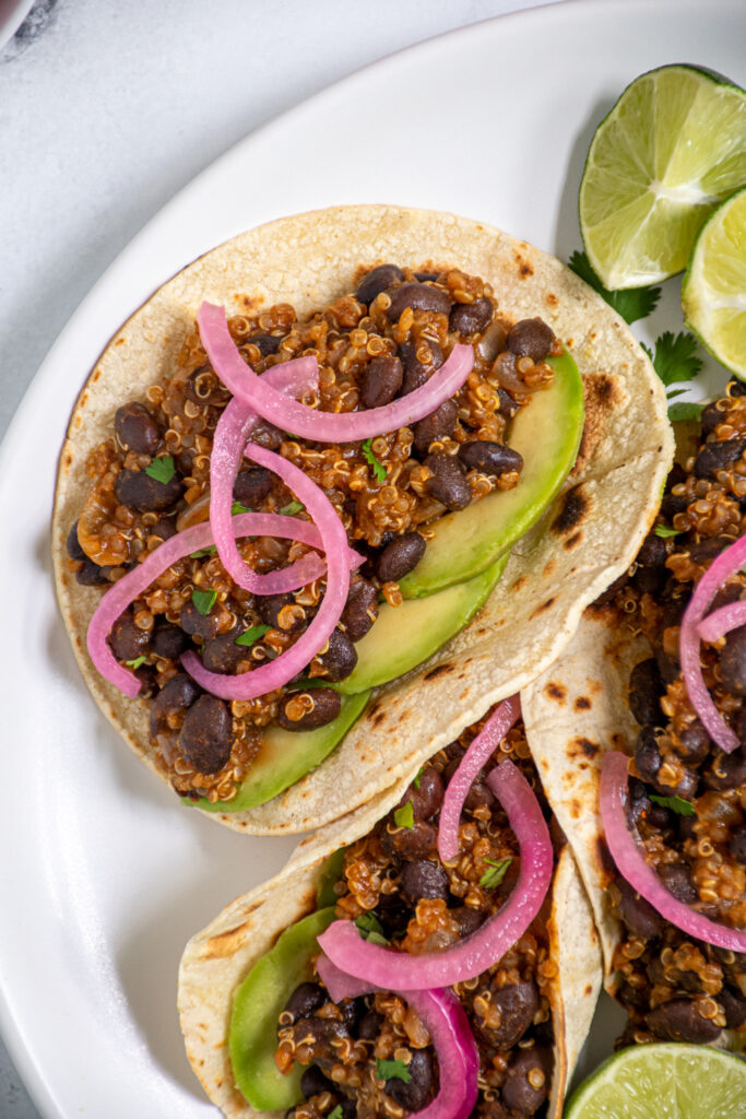 Overhead view of a close up of a corn tortilla filled with black bean quinoa taco meat garnished with cilantro, pickled red onions, and avocado.