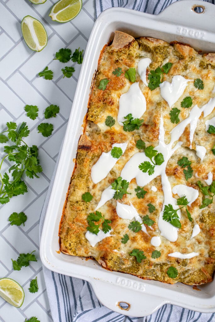 Overhead close up view of baked green chicken enchiladas topped with melted cheese, sour cream, and cilantro.