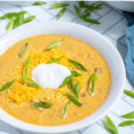 Pinterest Pin with text 'Crockpot Creamy Pumpkin Chili', image a bowl of yellow pumpkin chili topped with green onions, and sour cream.