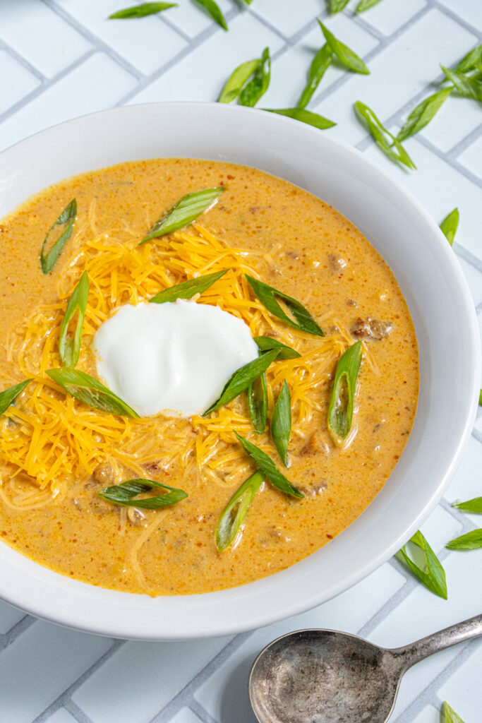 White bowl against a white background filled with yellow crockpot pumpkin chili garnished with green onions and sour cream.
