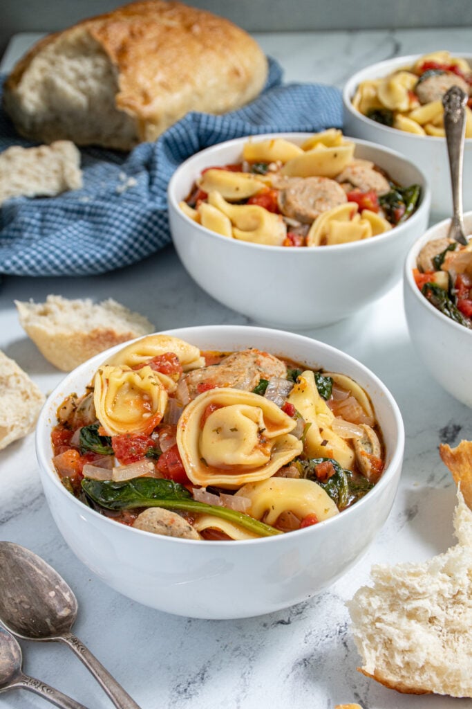 White bowl with chicken sausage tortellini soup with tomatoes and spinach.