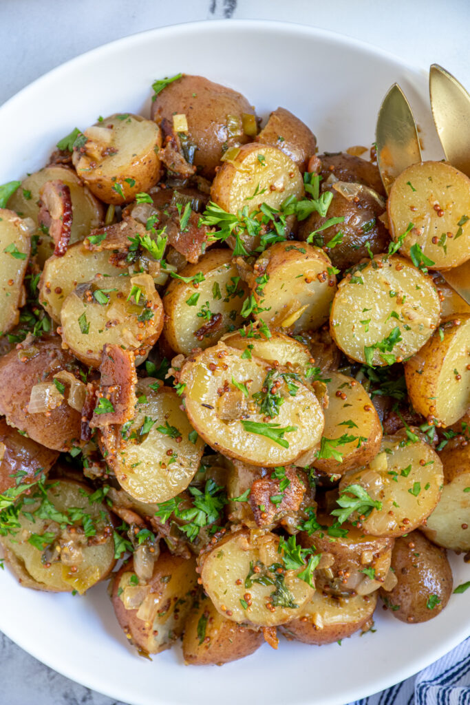 Close up view of German Potato Salad show potatoes in a mustard sauce with bacon and parsley.