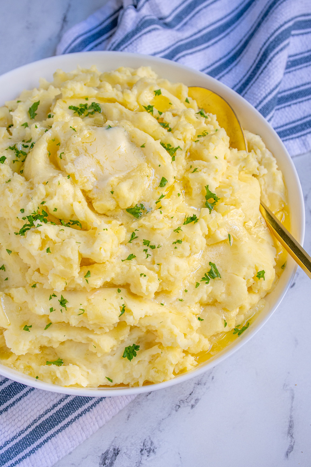 White bowl full of fluffy mashed potatoes dripping with melted butter and garnished with fresh parsley.