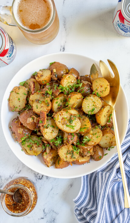 Overhead of a white bowl full of warm German potato salad with whole grain mustard, bacon, and fresh parsley.