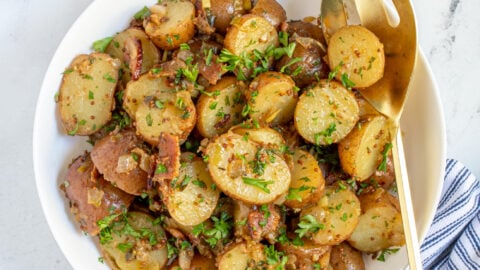 Overhead of a white bowl full of warm German potato salad with whole grain mustard, bacon, and fresh parsley.