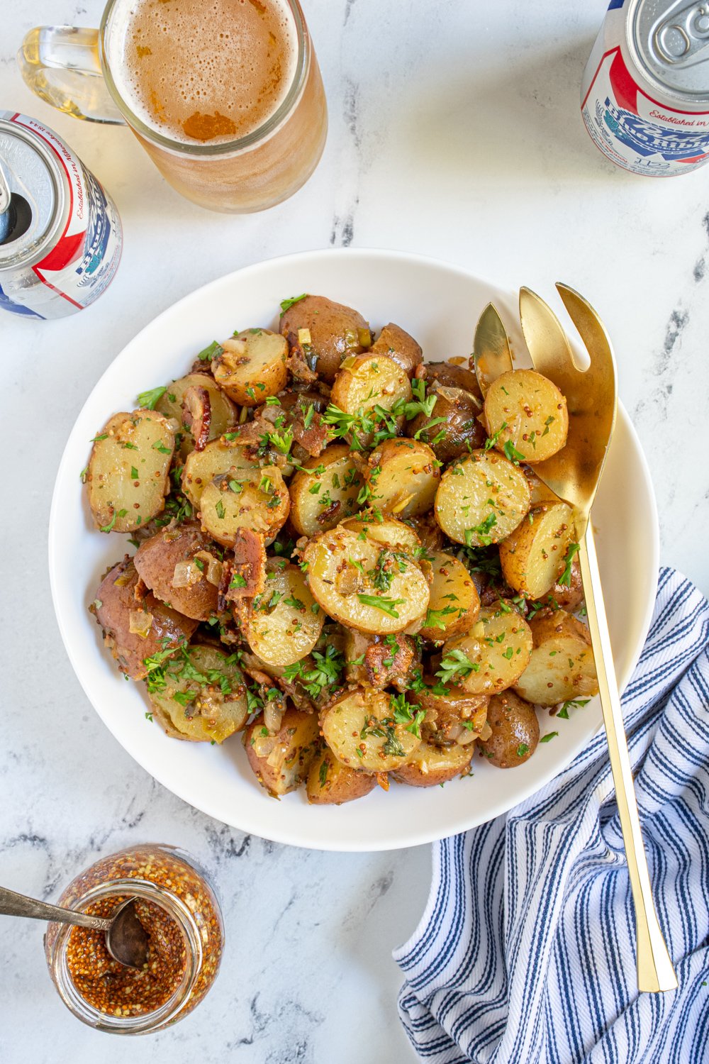 Overhead of a white bowl full of warm German potato salad with whole grain mustard, bacon, and fresh parsley.
