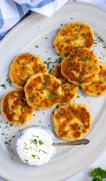 Platter full of golden brown and crispy leftover mashed potato cakes garnished with parsley and next to sour cream.