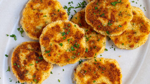 Platter full of golden brown and crispy leftover mashed potato cakes garnished with parsley and next to sour cream.