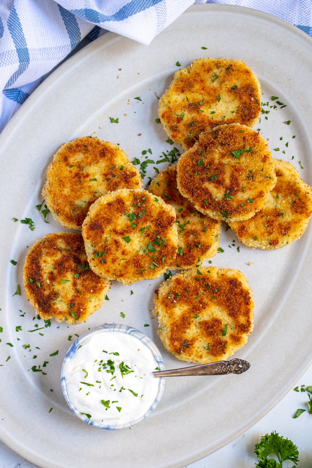 Platter full of golden brown and crispy leftover mashed potato cakes garnished with parsley and next to sour cream.