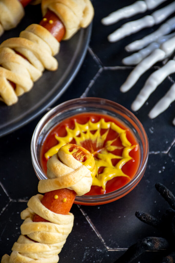 A mummy dog that has been dipped in ketchup and mustard.