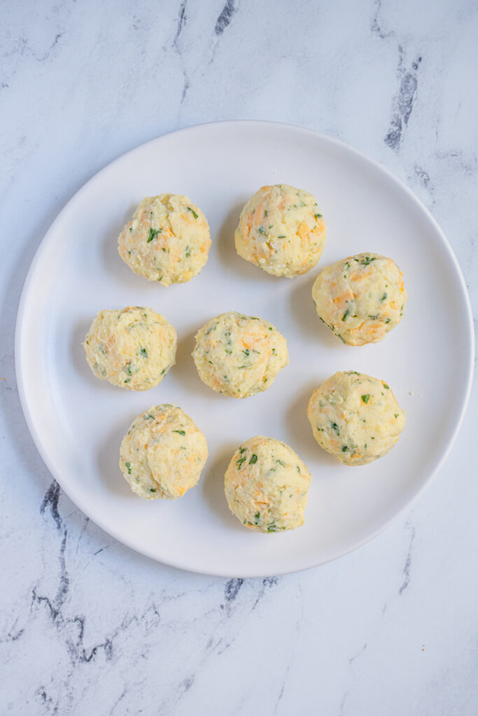 Balls of leftover mashed potato mixture laid on a white plate.