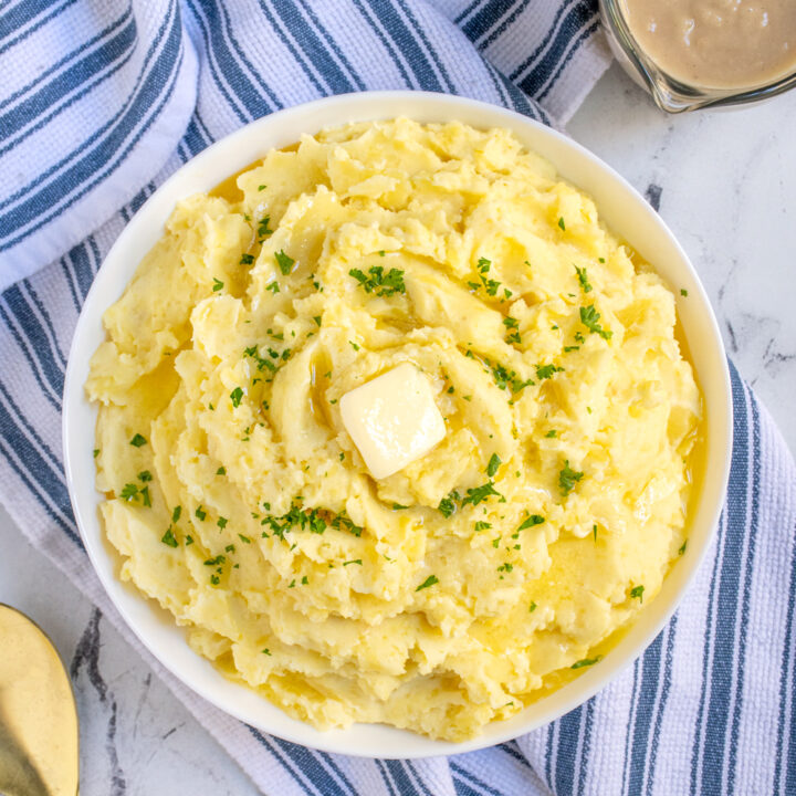 Overhead view of a large bowl of classic mashed potatoes top with a slab of butter and garnished with fresh parsley.