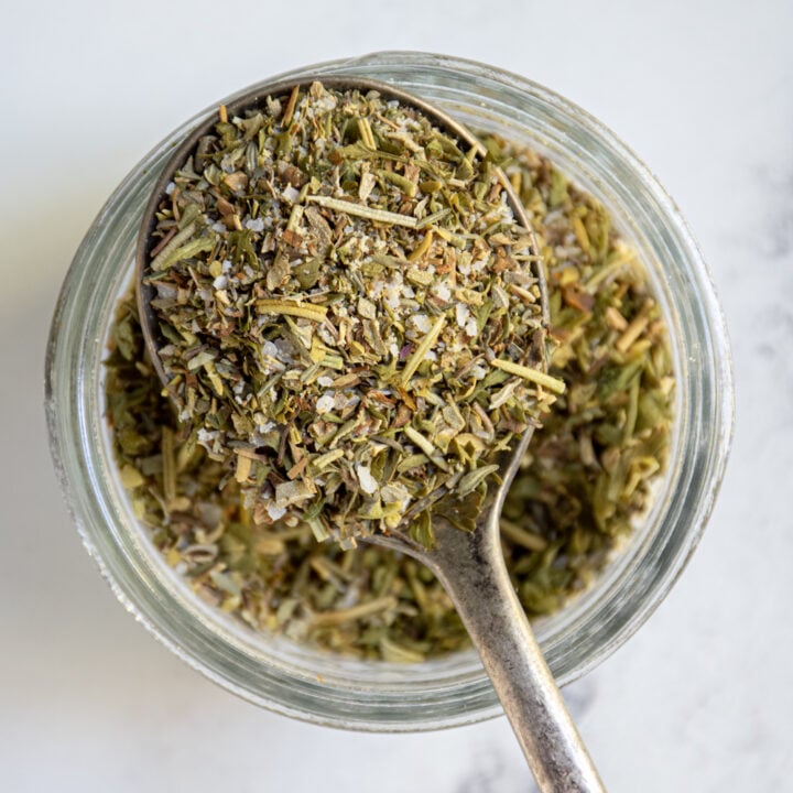 Overhead view of Italian seasoning in a spoon that is resting on a little jar.