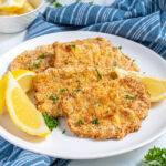Pinterest Pin with text 'Air Fryer Pork Schnitzel', image of a white plate full of golden brown schnitzel garnished with parsley and lemon wedges.