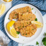 Pinterest Pin with text 'Air Fryer Pork Schnitzel', image of a white plate full of golden brown schnitzel garnished with parsley and lemon wedges.