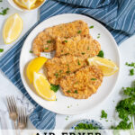 Pinterest Pin with text 'Air Fryer Pork Schnitzel', image of a white plate full of golden brown schnitzel garnished with parsley and lemon wedges.