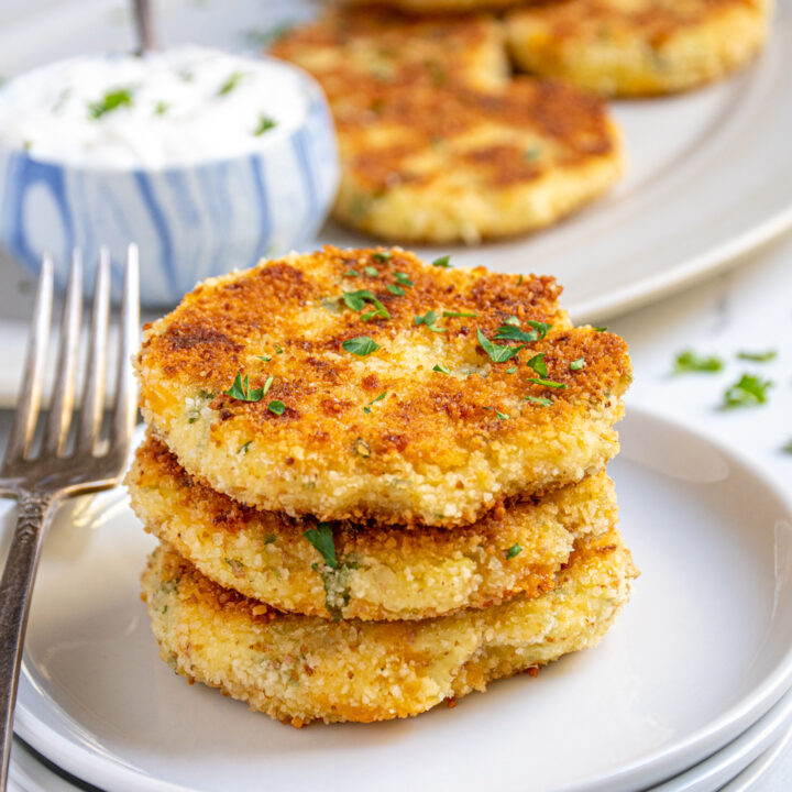 Three golden brown mashed potato cakes staked on a plate next to a fork.