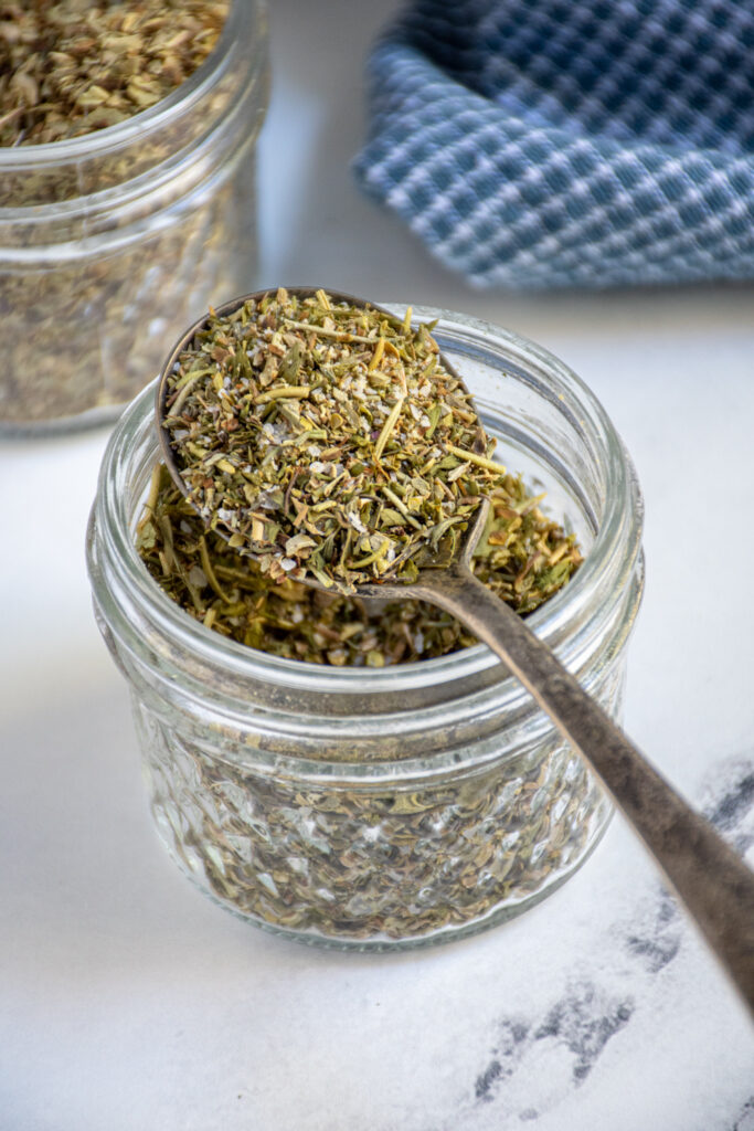 A jar and spoon full of homemade Italian spice blend.