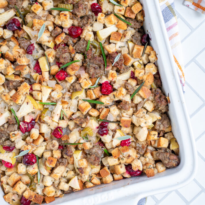 Overhead photo of an angled white dish with stuffing filled with sausage, cranberries, and apples.