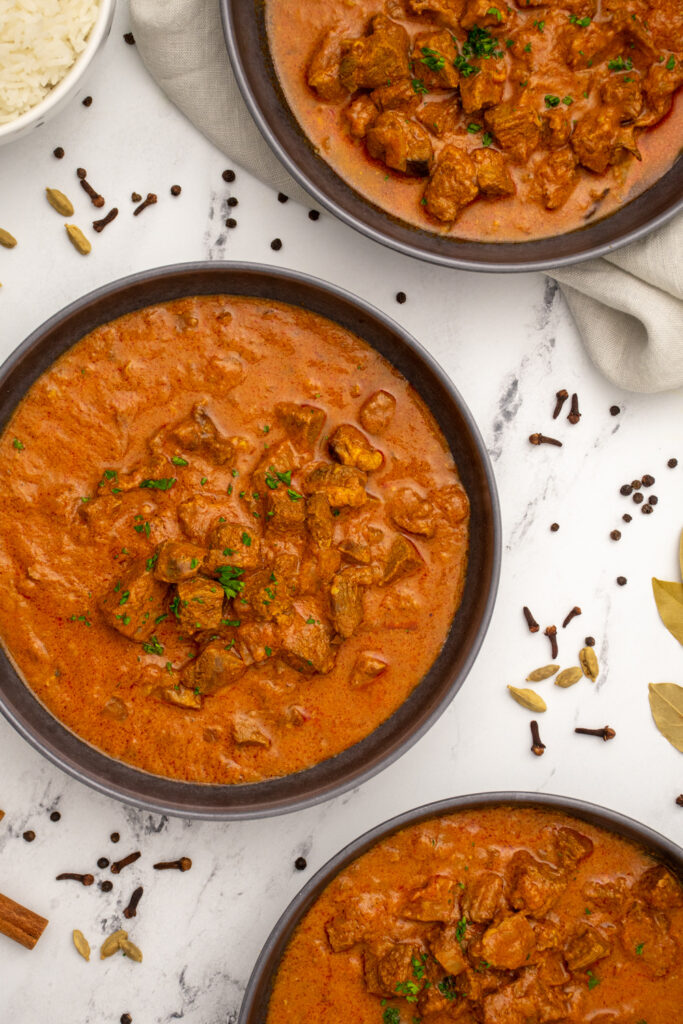 Close up of a black bowl of lamb curry showing off big pieces of lamb garnished with fresh parsley.