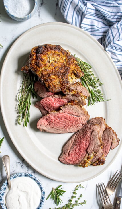 Overhead view of a roasted boneless leg of lamb on a platter, half of it sliced open revealing a tender pink inside.