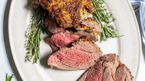 Overhead view of a roasted boneless leg of lamb on a platter, half of it sliced open revealing a tender pink inside.