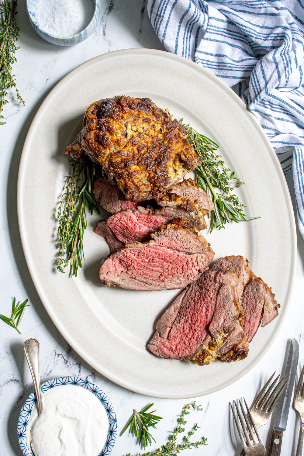 Overhead view of a roasted boneless leg of lamb on a platter, half of it sliced open revealing a tender pink inside.
