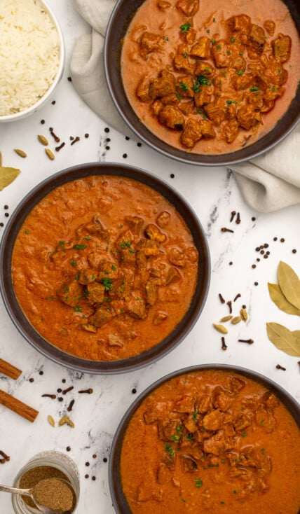 Three black bowls on a table filled with leftover lamb curry, showing chunks of tender lamb and garnished with parsley.
