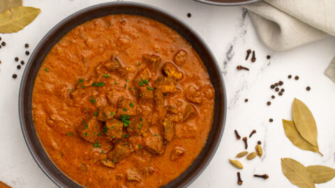 Three black bowls on a table filled with leftover lamb curry, showing chunks of tender lamb and garnished with parsley.