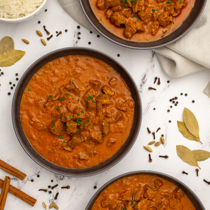 Three black bowls on a table filled with leftover lamb curry, showing chunks of tender lamb and garnished with parsley.