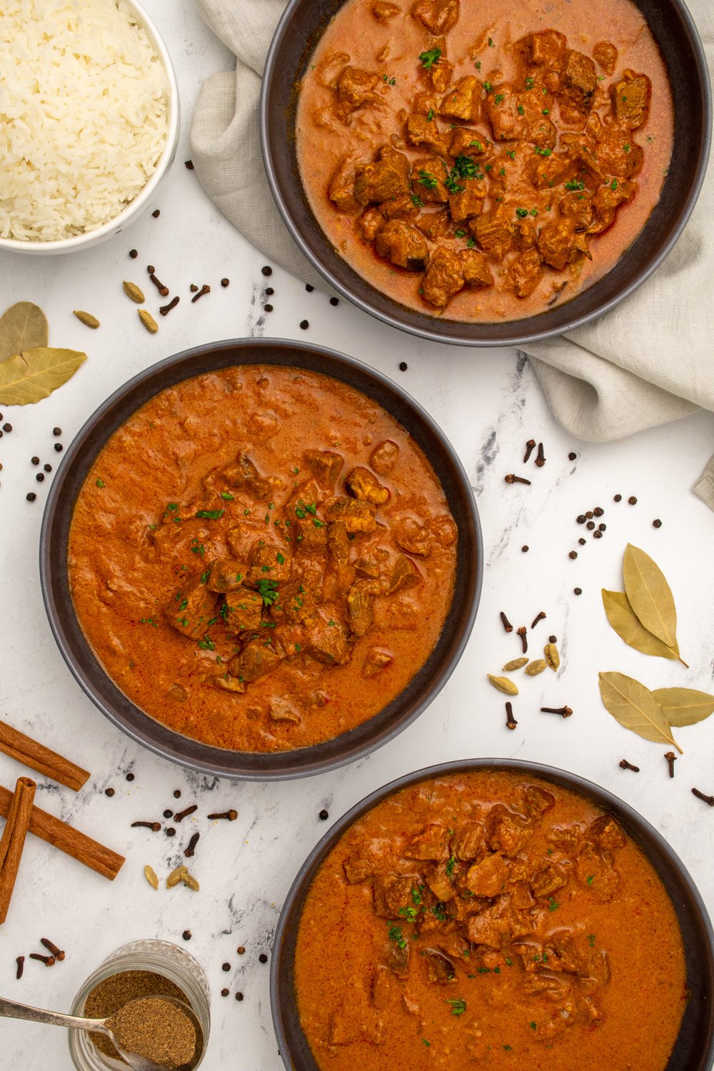Three black bowls on a table filled with leftover lamb curry, showing chunks of tender lamb and garnished with parsley.