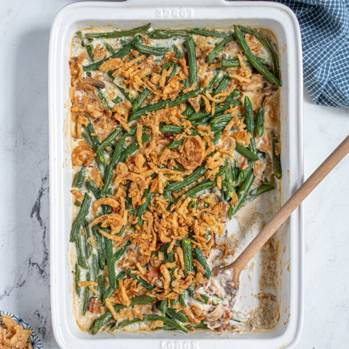 Overhead view of a white casserole dish with homemade green bean casserole with a serving spoon and some on a plate next to it.