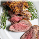 Pinterest Pin with text 'Roasted Boneless Leg of Lamb', image of roasted lamb on a platter with slices showing off a pink tender center.