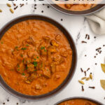 Pinterest Pin with text 'Leftover Lamb Curry', image of three black bowls filled with curry garnished with parsley.