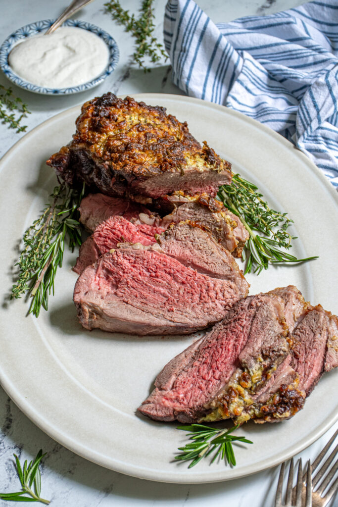 A boneless leg of lamb roasted to perfection on a large platter, half of it cut open into slices showing off a tender pink inside.